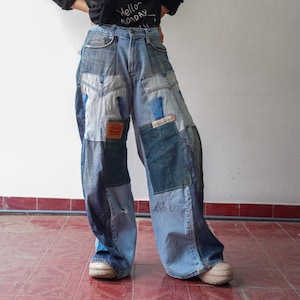 Könnte beinhalten: Weite Jeanshose im Patchwork-Design aus blauem Denim. Die Hose hat ein Patchwork-Design mit verschiedenen Blautönen, ein rotes Levi's-Etikett und einen Used-Look. Dazu wird ein schwarzes T-Shirt mit dem Text "Hello Monday" getragen.