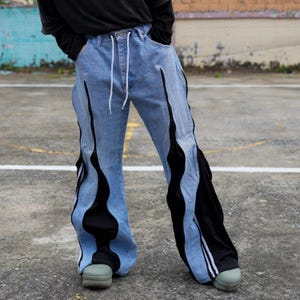 May include: Light blue denim jeans with black flame-like accents down the sides. The jeans have a drawstring waist and are paired with green platform shoes. The black accents have white stripes.