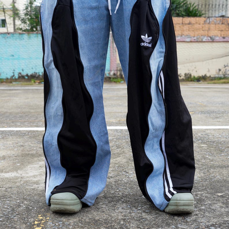 May include: Light blue denim pants with black side panels and white stripes. The pants feature the Adidas logo and a drawstring. The bottom of the pants are over the green shoes.