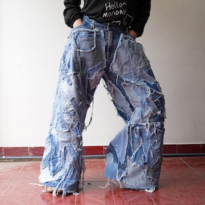 Peut inclure: Jean bleu avec un design patchwork. Le jean présente plusieurs couches de patchs en denim, créant un look unique et vieilli. Le jean a une jambe large et une taille haute. La personne sur l'image porte un t-shirt noir à manches longues avec le texte "Hello Monday".