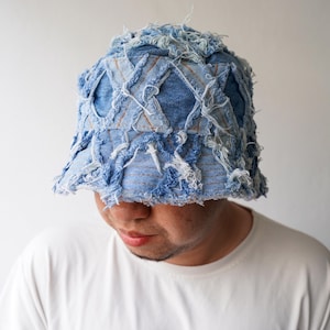 Könnte beinhalten: Ein hellblauer Jeans-Eimerhut mit einem Used-Patchwork-Design. Der Hut hat ausgefranste Kanten und eine einzigartige Textur, die eine Mischung aus hell- und mittelblauem Denim zeigt. Ein stilvolles Accessoire.