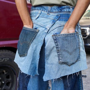May include: A denim skirt made from multiple pieces of blue denim, with raw edges and frayed hems. The skirt has two large pockets on the back, one on each side.