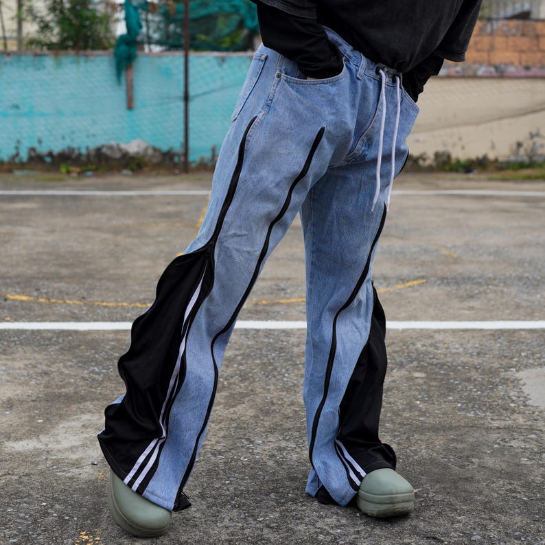 May include: Light blue denim pants with black side panels and white stripes. The pants have a drawstring waist and are worn with green shoes. The design features a unique combination of denim and contrasting fabric.