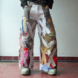 以下が含まれることがあります： ユニークなデザインのパッチワークデニムパンツ。グレー、白、カラフルな生地のパッチが混ざり合い、ワイドレッグフィットになっています。パッチは抽象的なパターンで配置され、大胆で芸術的な外観を作り出しています。パンツは、明るい緑色の靴と合わせています。