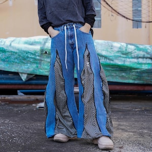 Può includere: Jeans di denim blu con un motivo geometrico bianco e nero sui lati. I jeans hanno una gamba larga e sono tagliati sopra la caviglia.