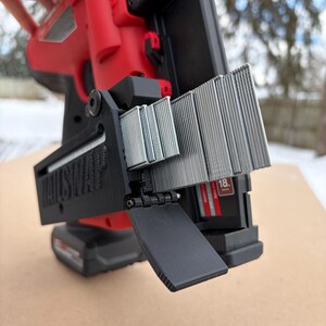 May include: A red and black nail gun with a black magazine loaded with silver nails. The nail gun is held by a hand, with the text "NAILSHAPE" visible on the magazine.