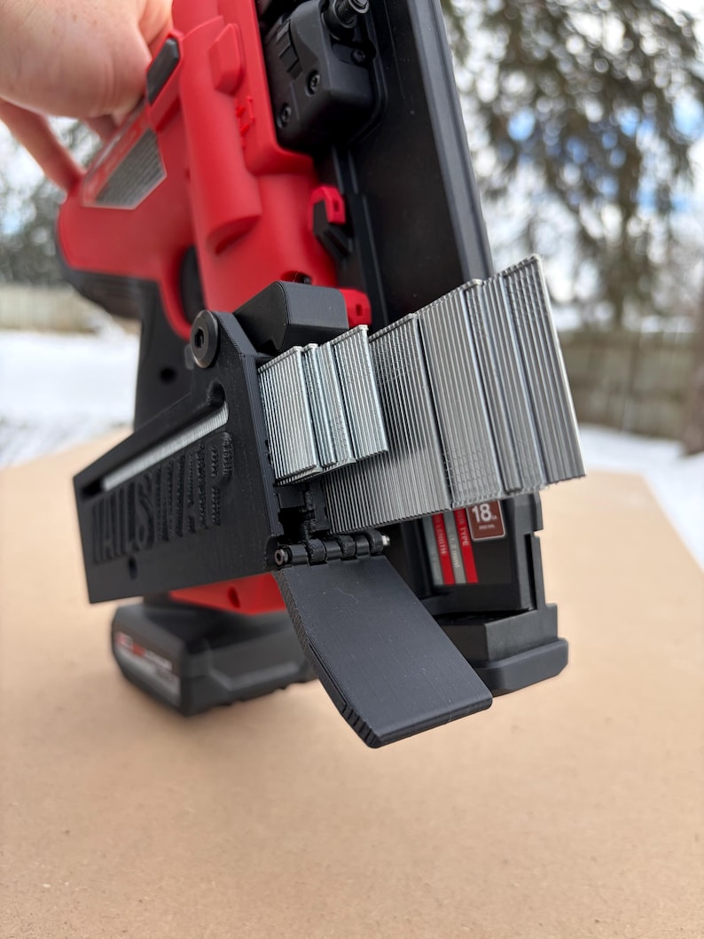 May include: A red and black nail gun with a black magazine loaded with silver nails. The nail gun is held by a hand, with the text "NAILSHAPE" visible on the magazine.