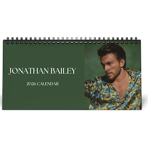 May include: A spiral-bound desk calendar featuring a photograph of Jonathan Bailey. The calendar has a dark green cover with the name "JONATHAN BAILEY" and the year "2026 CALENDAR" printed in white. The right side of the calendar displays a color photo of Jonathan Bailey.