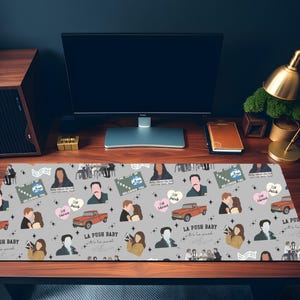 May include: A gray rectangular desk mat featuring a repeating pattern of illustrations and text. The design includes images of people, a red truck, and text that reads "LA PUSH BABY" and "Welcome to Forks".