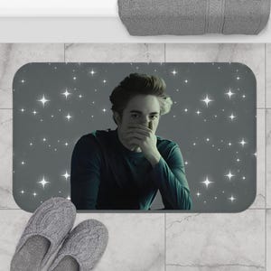 Puede incluir: Una alfombra de baño gris con un fondo estrellado gris oscuro y una imagen en blanco y negro de una persona con la mano cubriéndose la boca.