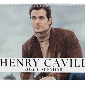 May include: A spiral-bound calendar featuring a portrait of Henry Cavill. He is wearing a brown suede jacket and a beige turtleneck. The calendar has the text "HENRY CAVILL 2026 CALENDAR" in a bold, black font across the bottom.