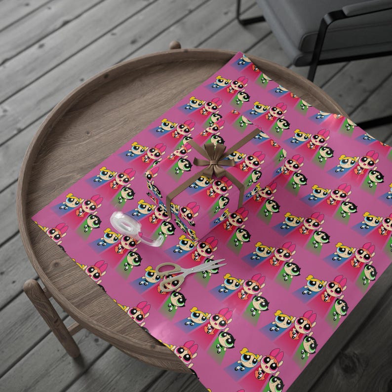 May include: A wrapped gift box and wrapping paper featuring a repeating pattern of cartoon characters on a pink background. The gift box is tied with a brown ribbon. A pair of scissors and a spool of ribbon are also visible.