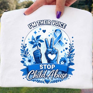 Peut inclure: Sac fourre-tout blanc avec un motif graphique bleu. Le motif comprend le texte "I'M THEIR VOICE" et "STOP Child Abuse". Le graphisme présente un signe de paix, un ruban, des fleurs et un moulinet, le tout dans des tons de bleu.