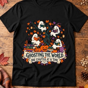 Peut inclure: Un t-shirt noir avec une illustration de quatre fantômes blancs lisant des livres dans un arbre entouré de feuilles d'automne, de citrouilles et de lanternes. Sous l'image, une bannière affiche le texte GHOSTING THE WORLD ONE CHAPTER AT A TIME.