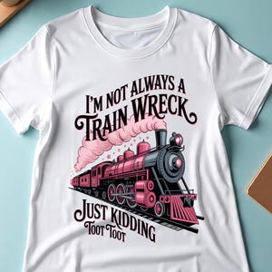 Peut inclure: T-shirt blanc avec un motif de train rose et noir et le texte "I'm Not Always a Train Wreck Just Kidding Toot Toot". Le motif représente une locomotive à vapeur avec de la fumée rose et des éléments décoratifs.