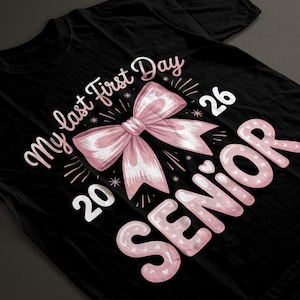 Peut inclure: T-shirt noir avec un nœud rose et le texte "My last first day 2026 Senior". Le motif comprend des cœurs et des éclats d'étoiles. Le t-shirt est fait d'une matière douce et confortable.