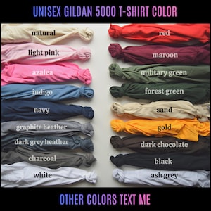 May include: A colour chart of Gildan 5000 unisex t-shirts. The image displays a variety of folded t-shirts in colours such as natural, light pink, azalea, indigo, navy, graphite heather, dark grey heather, charcoal, white, red, maroon, military green, forest green, sand, gold, dark chocolate, black, and ash grey.