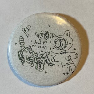 May include: A white button featuring a black and white line drawing of a monster with one eye and the text "I don't see the point".