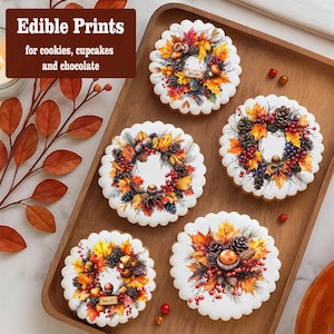 May include: Five round cookies with a scalloped edge are arranged on a wooden tray. Each cookie has a colourful autumn wreath design with leaves, berries, and pine cones. The text "Edible Prints" and "for cookies, cupcakes and chocolate" is displayed.