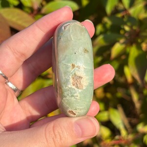 May include: A smooth, green and white polished stone with a rounded shape. The stone has a natural, organic look.