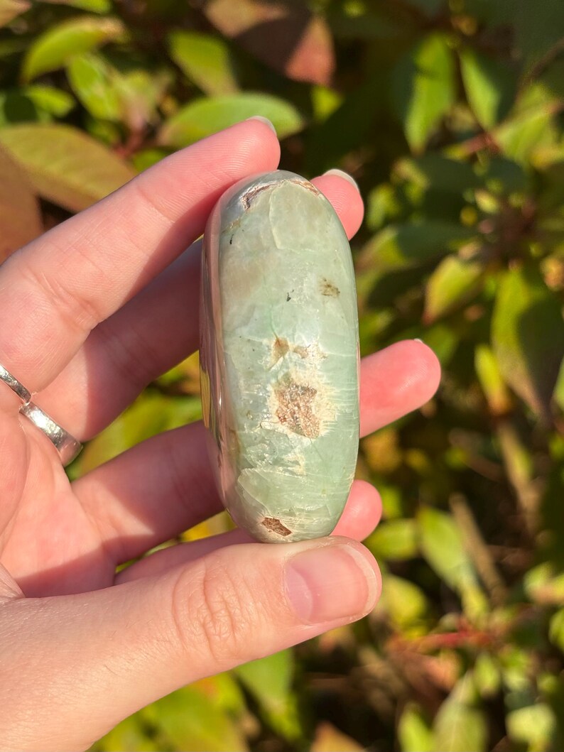 May include: A smooth, green and white polished stone with a rounded shape. The stone has a natural, organic look.