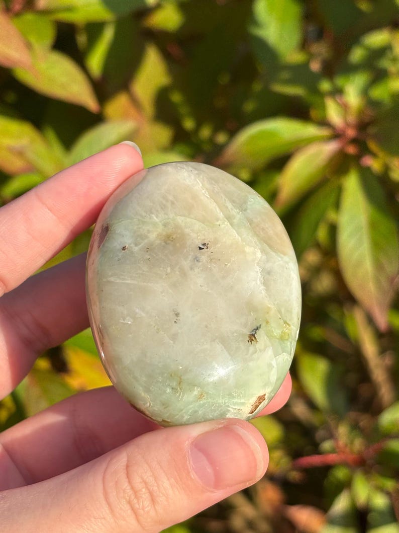 May include: A smooth, polished green and white gemstone with a rounded shape. The stone has a natural, organic look and is perfect for crystal healing or decoration.