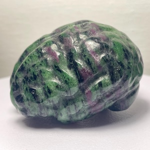 Peut inclure: Une sculpture de cerveau en pierre sculptée. Le cerveau est un mélange de couleurs vertes, noires et violettes. La sculpture est posée sur une surface blanche. Le cerveau est un objet décoratif unique.