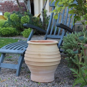 Peut inclure: Un grand pot en terre cuite de couleur terracotta avec une base arrondie et une large ouverture. Le pot est posé sur une surface de gravier devant une chaise en bois bleu.