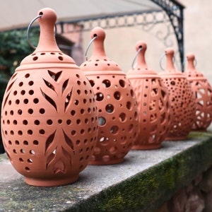 May include: Five terracotta candle lanterns with intricate cut-out designs. The lanterns are round and have a rustic, earthy look.