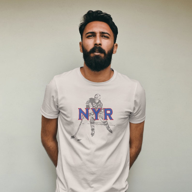 May include: White t-shirt with a vintage illustration of a hockey player and the text "NYR" in blue and red.