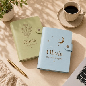 Può includere: Due diari personalizzati con chiusure a scatto, uno verde salvia con un motivo floreale e uno azzurro con una mezzaluna e stelle. Entrambi riportano il nome Olivia e il testo the next chapter stampato con un carattere marrone scuro.