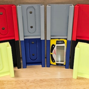 May include: Six wall-mounted storage holders in various colors, including red, gray, blue, and yellow. The holders are designed to hold small items, such as toy cars. One of the holders has a toy car inside.