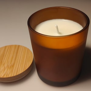 May include: A brown glass candle jar with a white wax candle inside. The jar has a wooden lid.