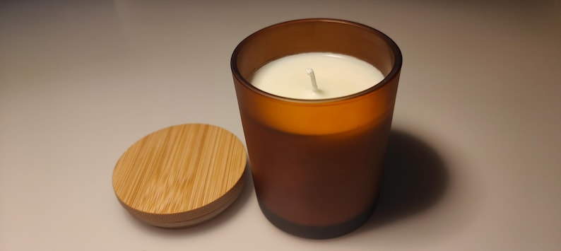 May include: A brown glass candle jar with a white wax candle inside. The jar has a wooden lid.