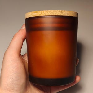May include: A brown frosted glass candle jar with a wooden lid. The candle is unlit.