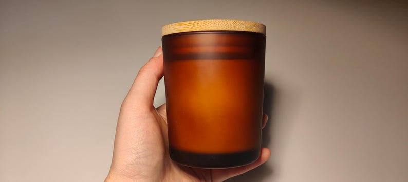 May include: A brown frosted glass candle jar with a wooden lid. The candle is unlit.
