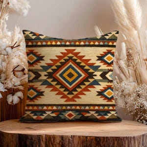 May include: A square throw pillow featuring a cream-colored base with a repeating geometric pattern in shades of burnt orange, navy blue, mustard yellow, and olive green, centered by a large diamond motif with horizontal border stripes.