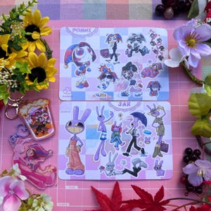 May include: Two rectangular sticker sheets featuring cartoon characters Pomni and Jax, alongside two acrylic keychains. The Pomni sheet displays various poses of a jester-like figure, while the Jax sheet shows a purple rabbit character.