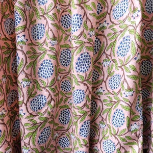 Peut inclure: Tissu rose avec un motif répété de grappes florales bleues, de feuilles vertes et de tiges marron. Le motif est imprimé sur un fond rose clair. Le tissu semble être un matériau de rideau ou de draperie.