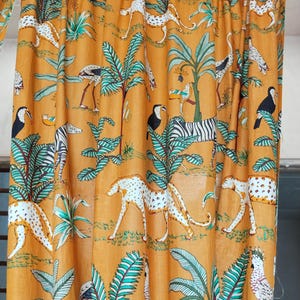 以下が含まれることがあります： マスタード色のカーテンパネル。ジャングルをテーマに、シマウマ、チーター、鳥、ヤシの木が描かれています。白、黒、ティールブルーのアクセントが特徴です。軽くて流れるような素材で、窓の装飾に適しています。