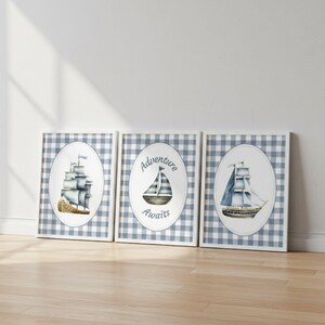Op de afbeelding: Set van drie ingelijste prints met aquarel illustraties van zeilboten. Elke print heeft een blauw-witte ruitjesachtergrond. Eén print zegt "Adventure Awaits". De zeilboten zijn in tinten blauw en bruin.
