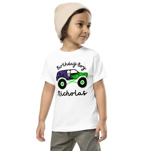 May include: White t-shirt with a green and purple monster truck graphic and the text "Birthday Boy Nicholas".