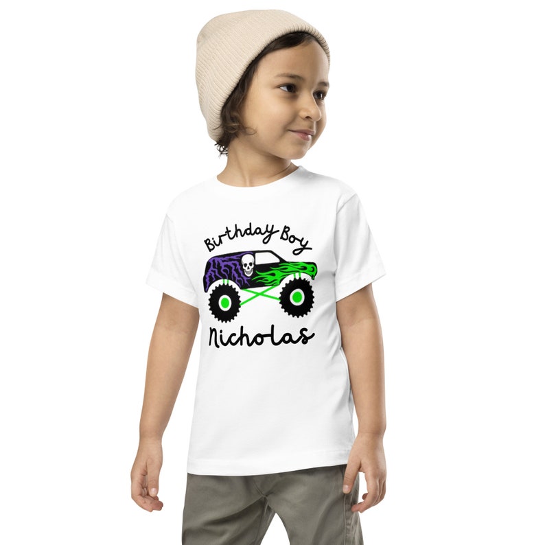 May include: White t-shirt with a green and purple monster truck graphic and the text "Birthday Boy Nicholas".