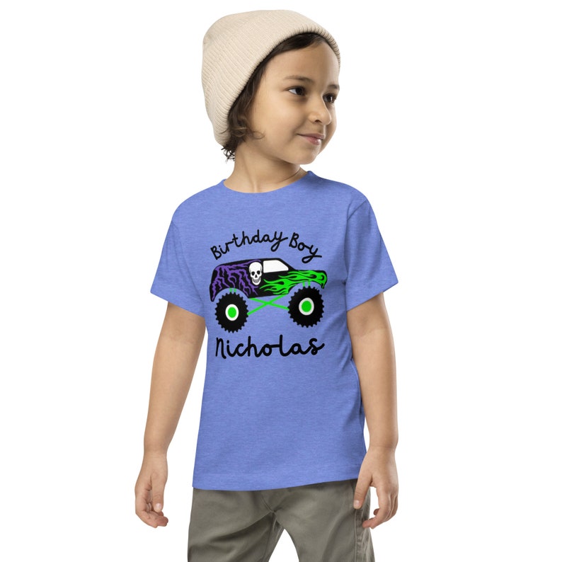 May include: A blue t-shirt with a green and purple monster truck graphic. The text "Birthday Boy Nicholas" is printed on the shirt.