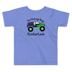 May include: A blue toddler t-shirt with a green monster truck graphic. The truck has a skull and flames. The text "Birthday Boy Nicholas" is printed on the shirt.