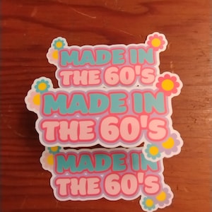 May include: Three stickers with the text "Made in the 60's" in a retro font. The stickers are pink, blue, and teal with yellow flower accents.
