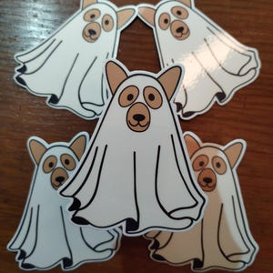 May include: Five white ghost stickers with brown dog faces. The ghosts are in various poses and have a simple, cartoon-like design.