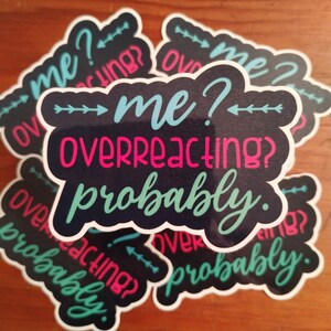 May include: A collection of stickers with a black background and white border. The stickers feature the text "me? overreacting? probably." in teal and pink script. The stickers are arranged on a wooden surface.