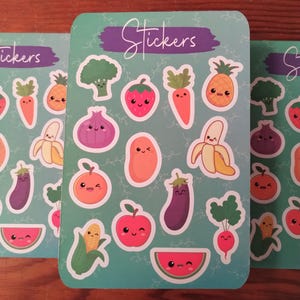 May include: A sheet of stickers featuring various fruits and vegetables with cute faces. The stickers are on a green background with white vines. The text "Stickers" is written in purple at the top of the sheet.
