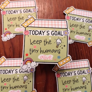 May include: Five green and white stickers with the text "TODAY'S GOAL keep the tiny humans alive" in black and white text. The stickers have a rainbow, a lightbulb, and hearts on them.